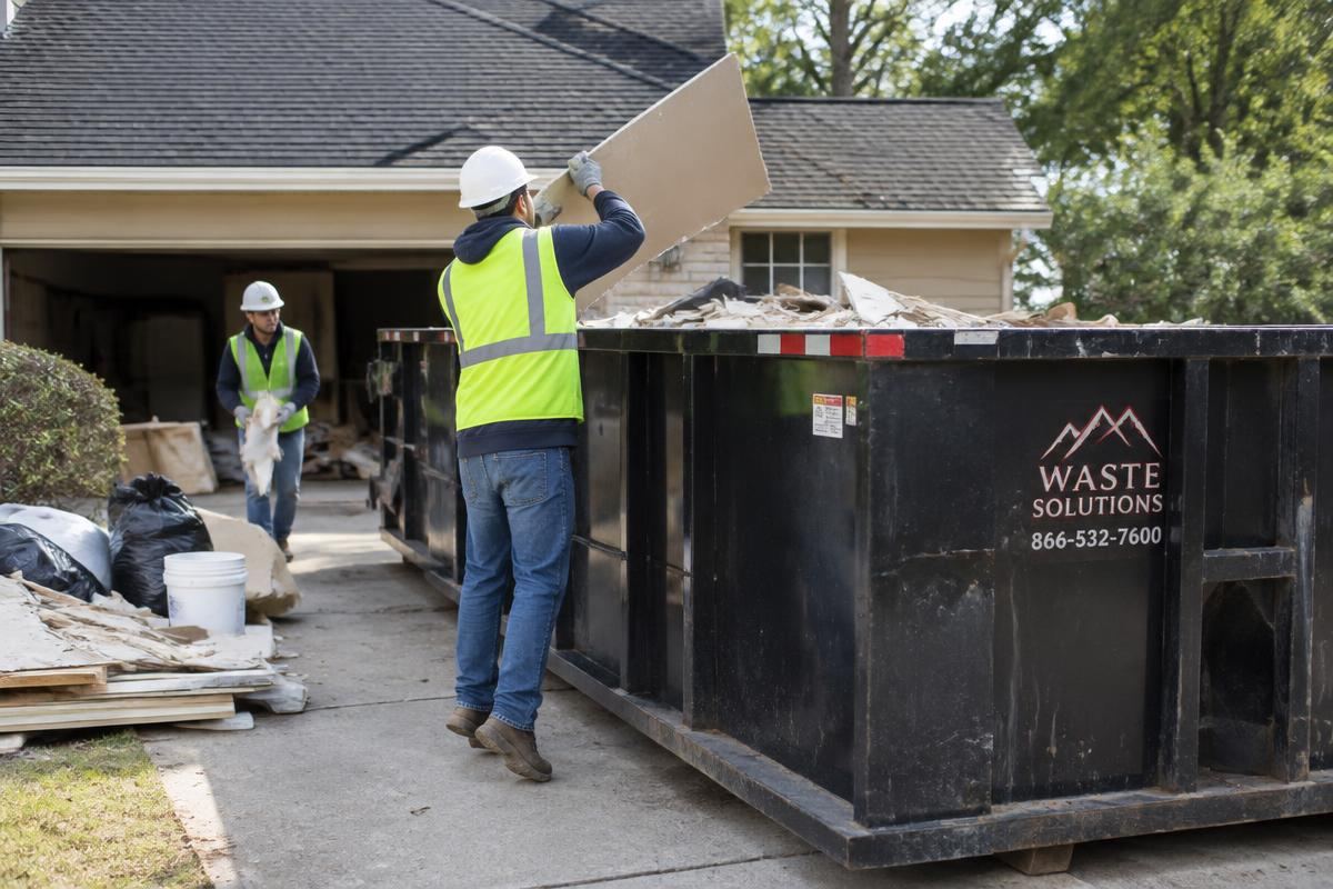 Workers loading renovation debris into a roll-off dumpster